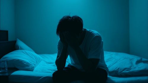 ベッドに座り頭を抱えてストレスを感じている男性
